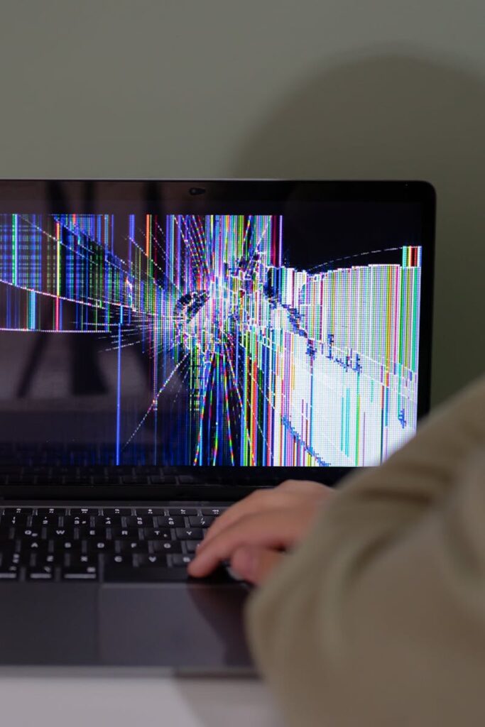 Individual viewing a laptop displaying a cracked and colorful digital screen indoors.